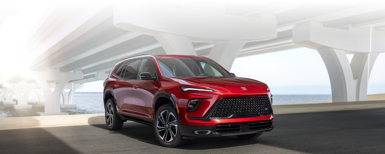 Front-side view of the 2025 Buick Enclave driving under a bridge at day.