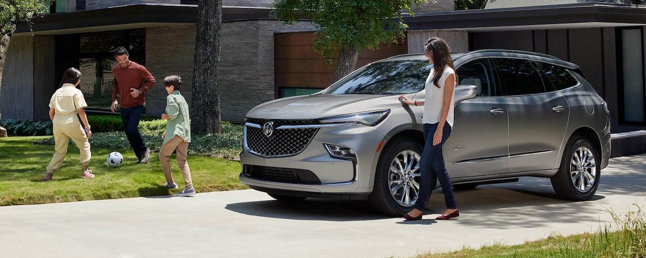 Buick Enclave Avenir 2024 stationné devant une maison dans une vue panoramique.