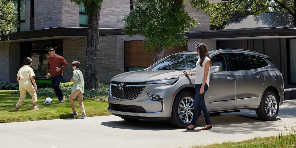 Buick Enclave Avenir 2024 stationné devant une maison dans une vue panoramique.