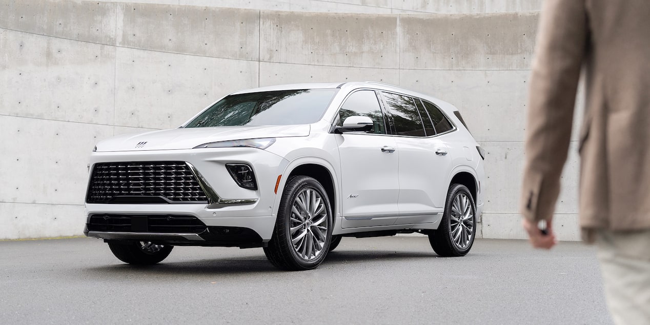 Vue latérale avant du Buick Enclave 2025 stationné à l’extérieur avec une personne qui passe à côté.