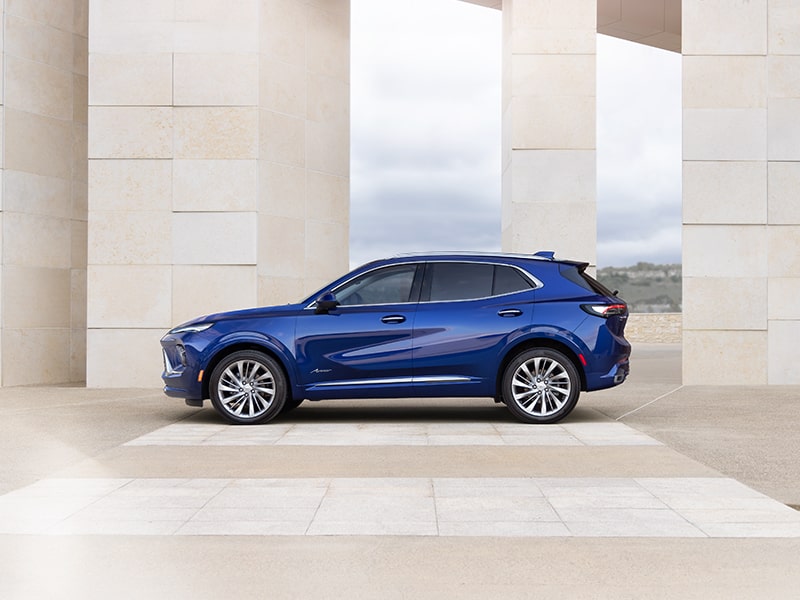 Side View of the 2025 Buick Envision Avenir Compact Luxury SUV Parked Near a Concrete Structure.