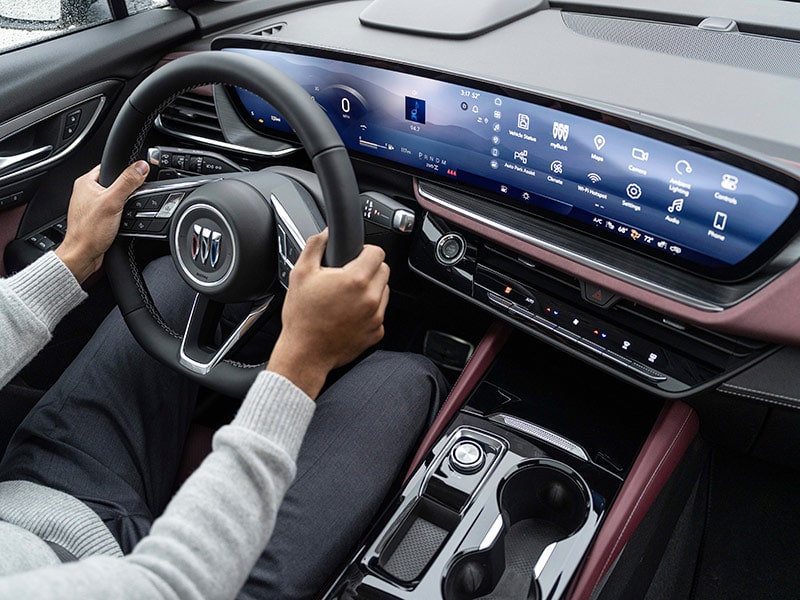 Front interiors of a 2025 Buick Envision Compact SUV with a Person Sitting in the Driver's Seat and Holding the Steering Wheel.